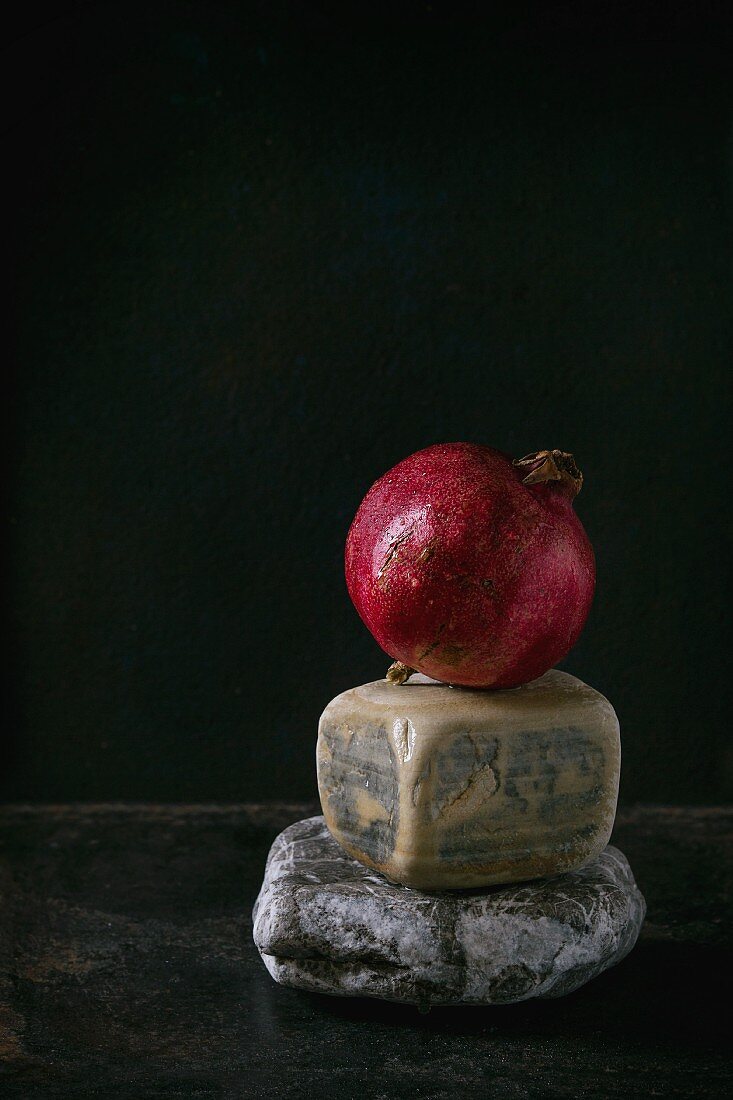 A whole pomegranate on decorative stones against a black background