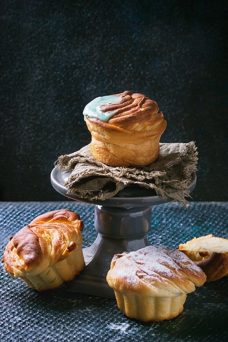 Selbstgemachte Cruffins (Croissant und Muffin) mit Zuckerglasur auf grauem Kuchenstander