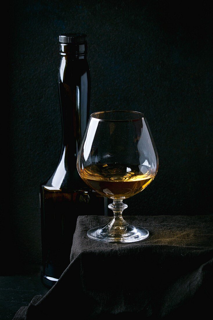 Bottle and glass of french apple calvados, standing on black tablecloth over balck background