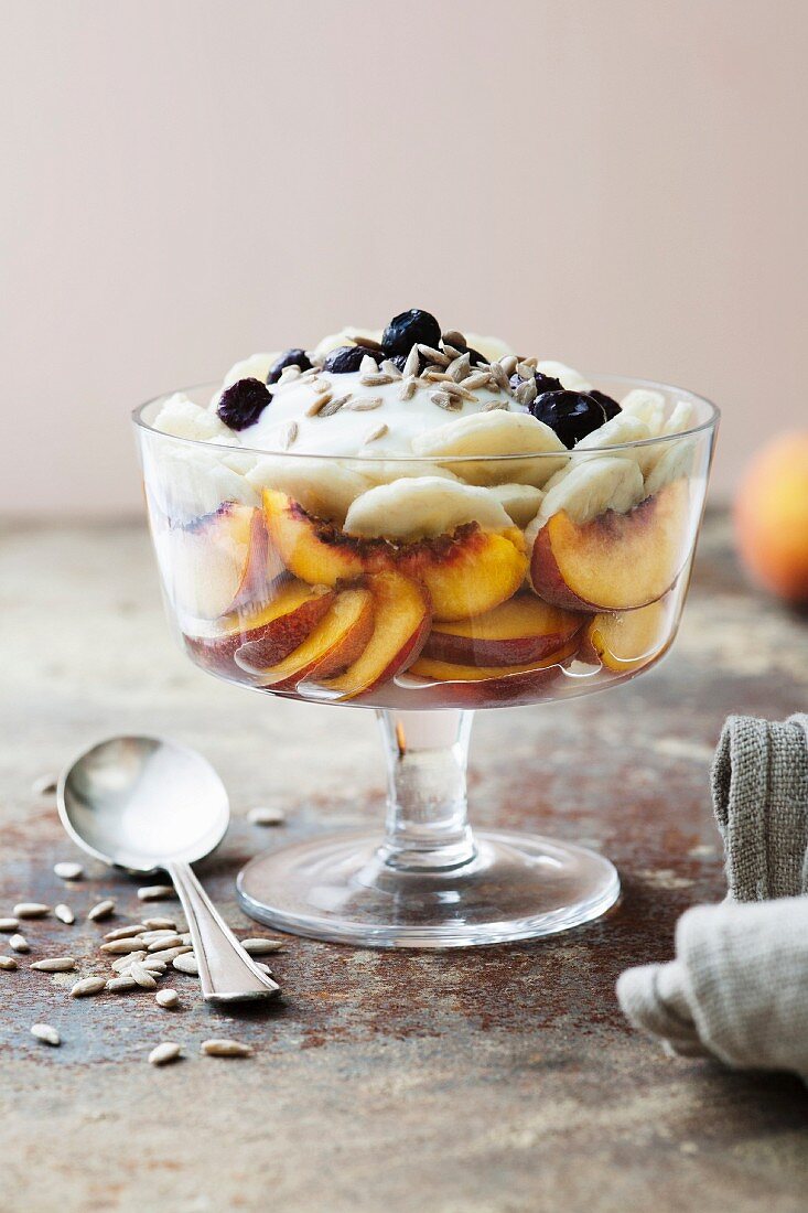 Healthy layered trifle – coconut yoghurt, sliced banana, peach, topped with sunflower seeds and blueberries