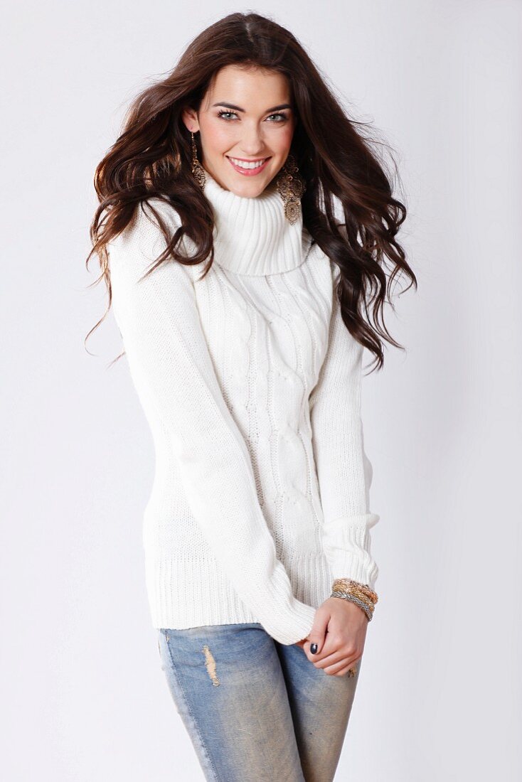 A brunette woman wearing a white cable-knit jumper and jeans