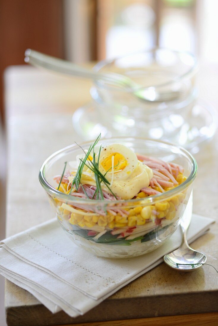 Layered salad with ham, corn, mayonnaise and egg