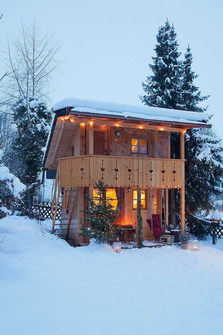 Alpine-style wooden cabin with illuminated interior in snowy garden