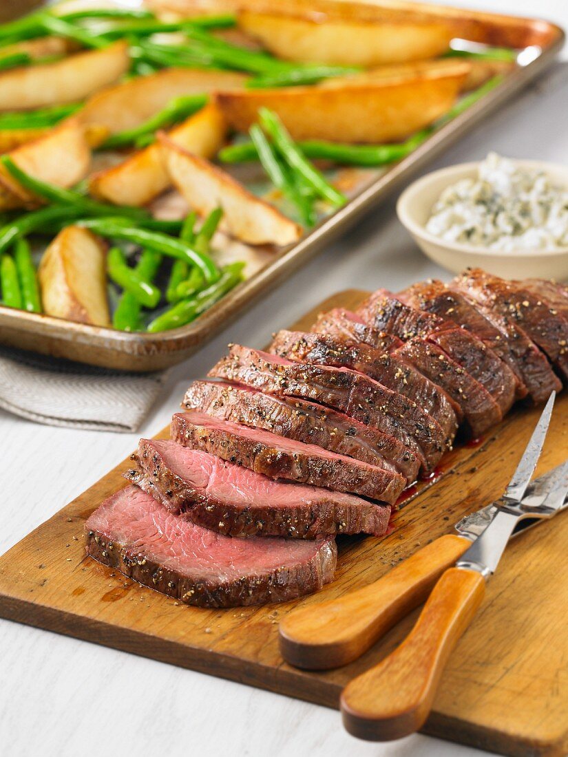 Roast beef with potatoes and green beans in front of a baking tray