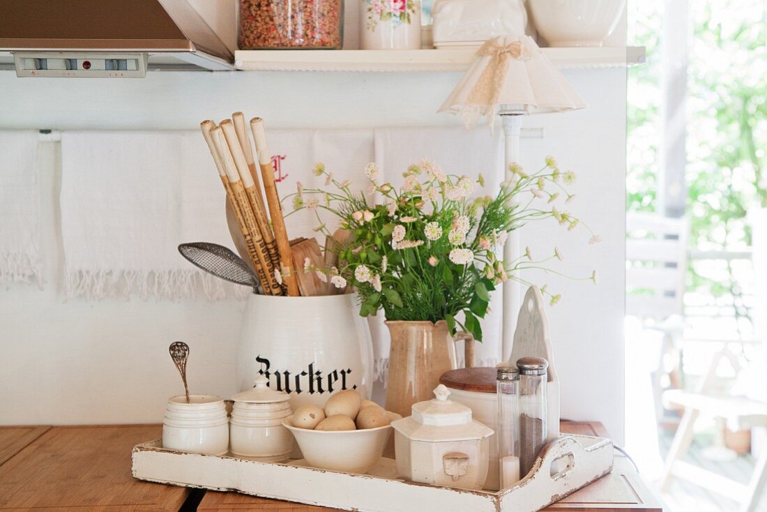 Kitchen utensils, sugar bowls and vase of flowers on white wooden tray