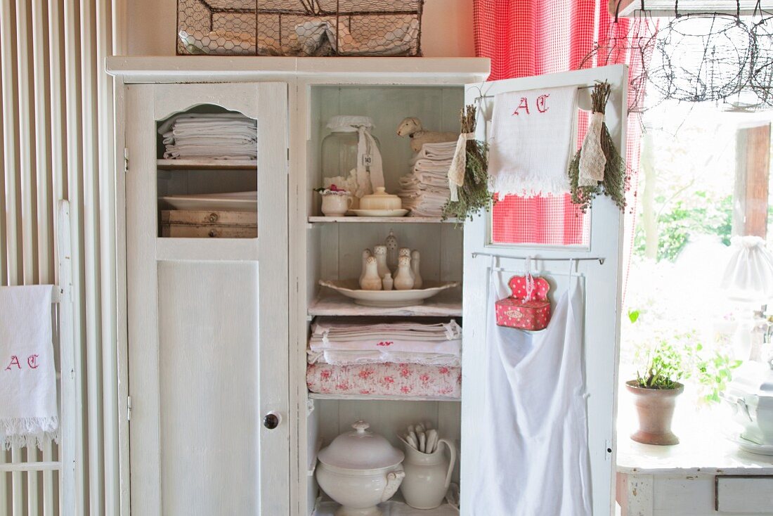 Table linen and kitchen utensils in old cupboard with open door