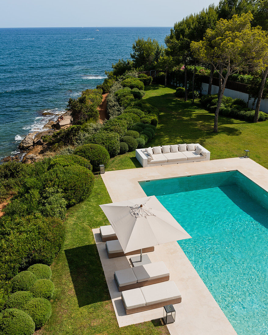 View down onto pool with loungers and manicured garden next to the sea