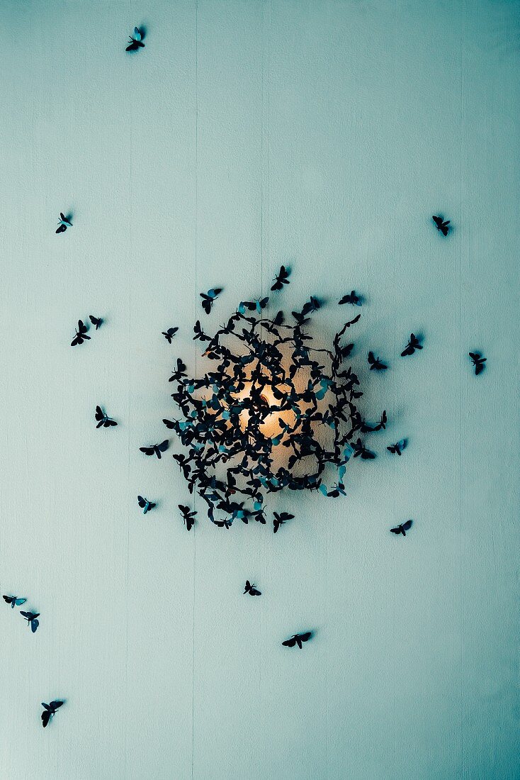 A wall light surrounded by a swarm of fake moths designed by Katharina Mischer and Thomas Traxler