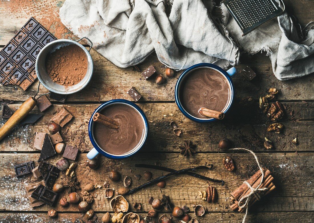 Heiße Schokolade mit Zimt in zwei Bechern, Anis, Nüsse und Kakaopulver auf rustikalem Holzuntergrund