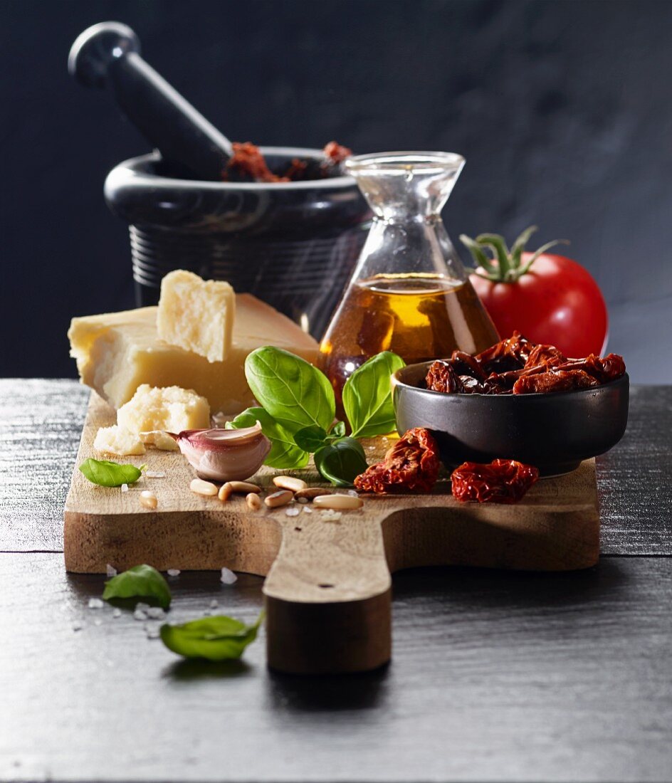 Stillleben mit Tomaten, Olivenöl, Parmesan, Knoblauch, Pinienkernen und Basilikum auf Schneidebrett