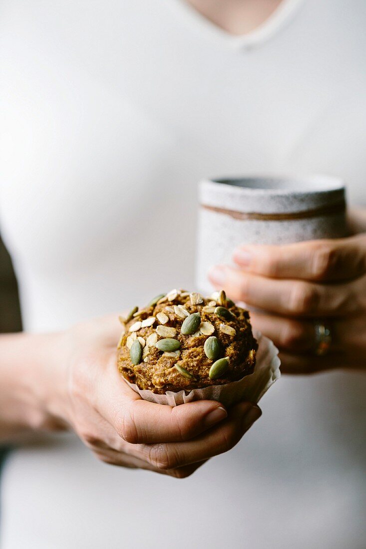 A woman is holding a freshly baked Maple Sweetened Pumpkin Oat Muffin in her hand