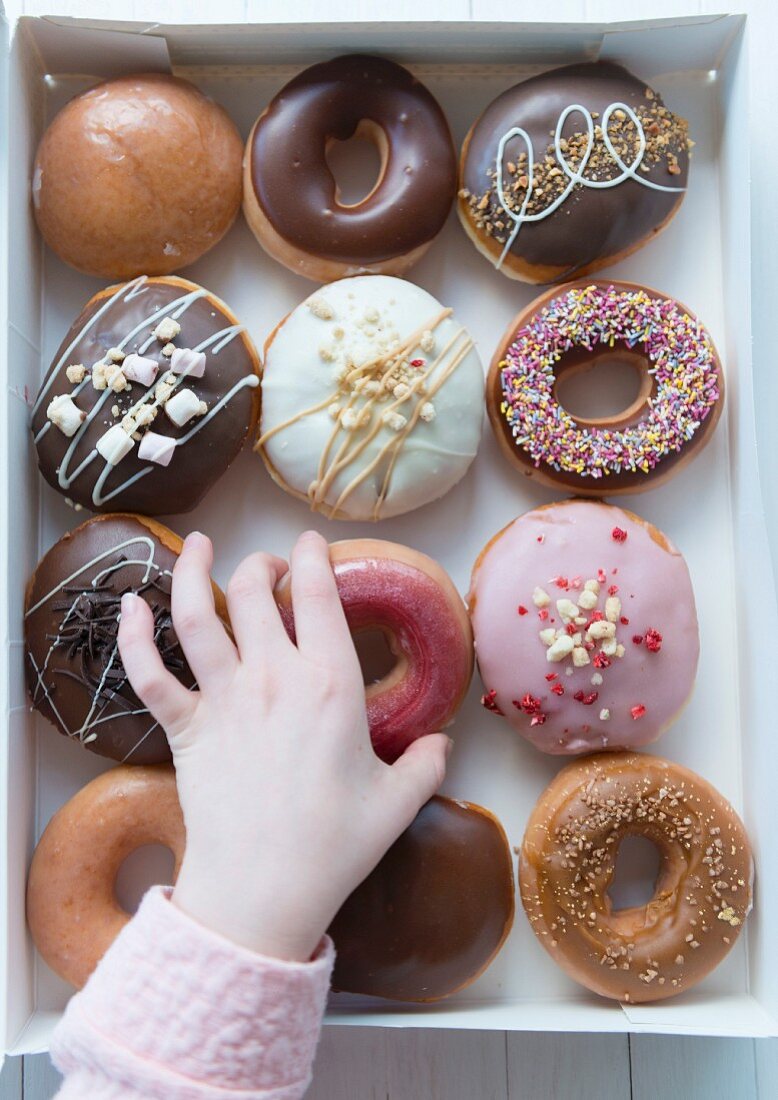 A hand selecting a donut from a box of a dozen donuts