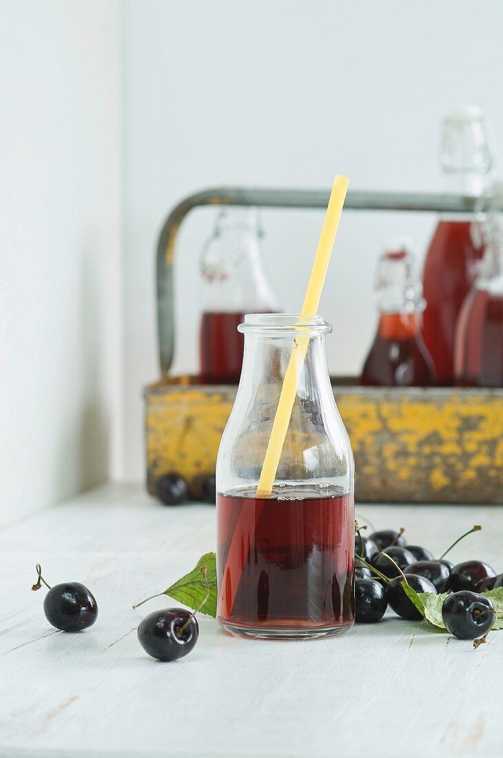 Kirschsaft im Glas mit Trinkhalm, Flaschen im Träger und frische Kirschen