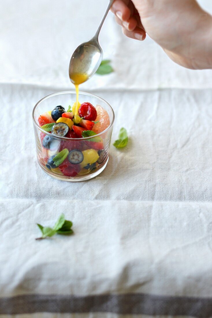 A fruit salad being drizzled in a basil and mint citrus syrup