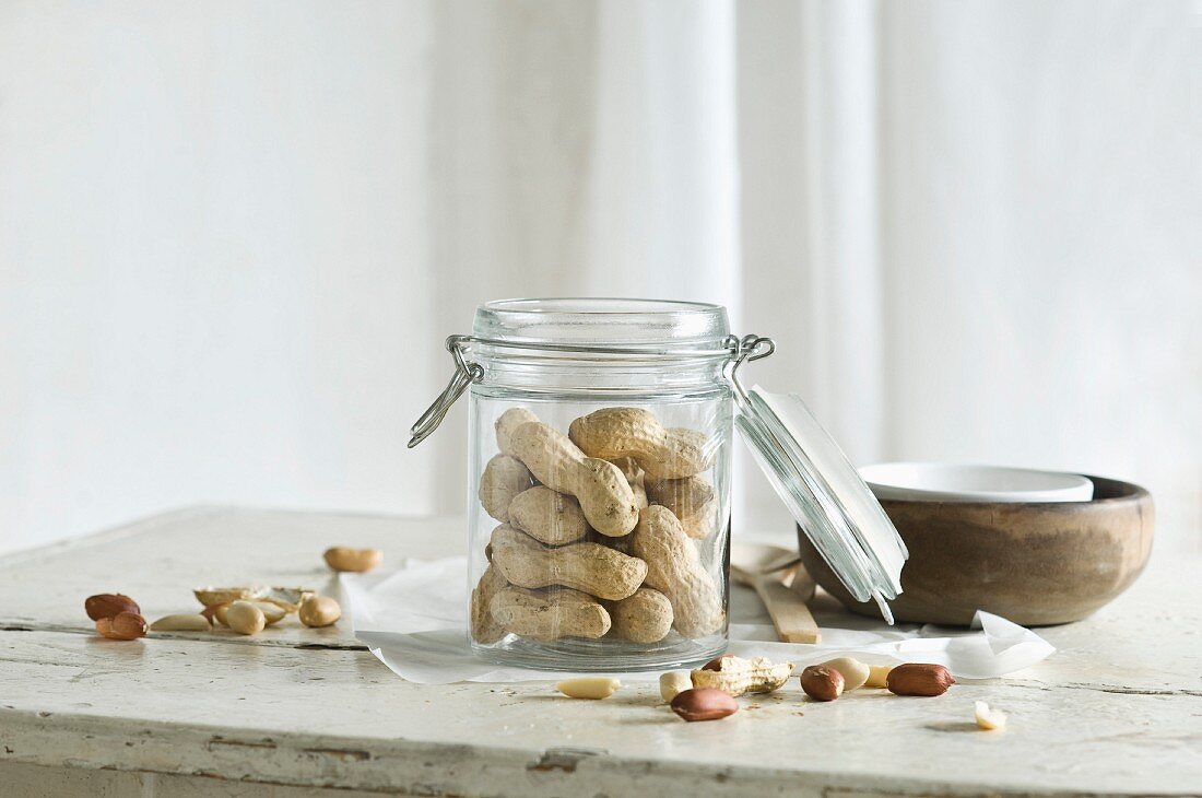 Erdnüsse im Vorratsglas und daneben auf rustikalem Küchentisch