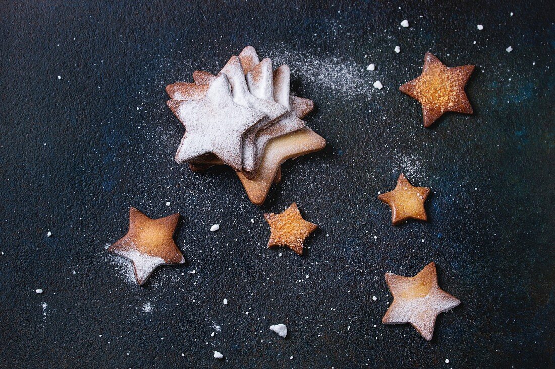 Homemade shortbread star shape sugar cookies different size with sugar powder on black textural surface