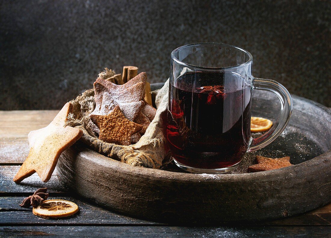 Glass mug of hot red mulled wine spices, sugar shortbread cookies star shape, anise and cinnamon powder in clay tray