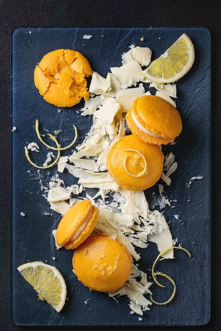 Orangen-Zitronen-Macarons mit weißen Schokoladenspänen auf dunklem Untergrund