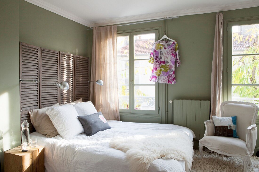 Olivgrünes Schlafzimmer mit Paravent als Betthaupt und Schaffell auf Doppelbett