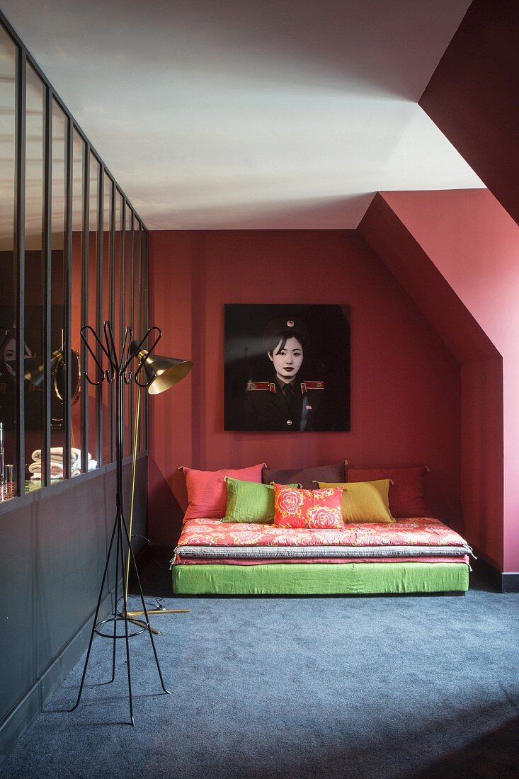 Bett mit verschiedenen Matratzen und Kissen vor mauvefarbener Wand mit Frauenfotografie