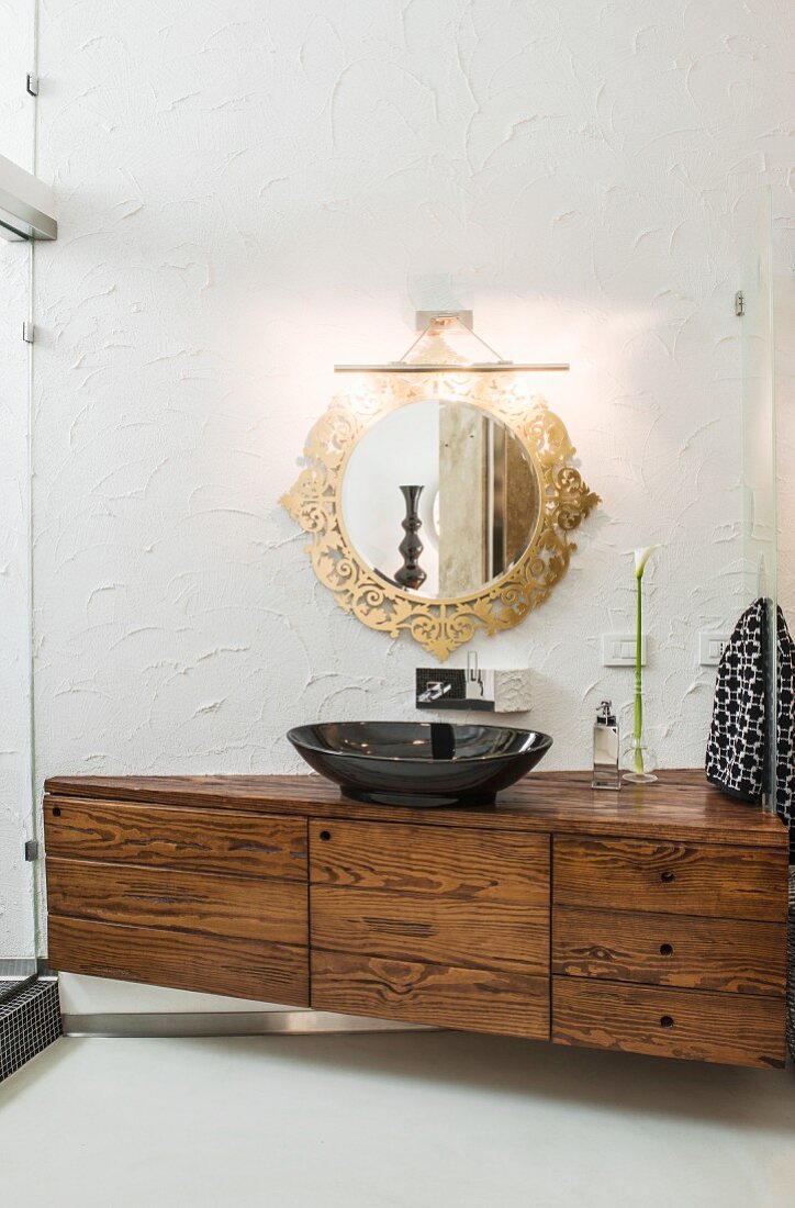 Black sink on elegant washstand below round mirror with ornate gilt frame