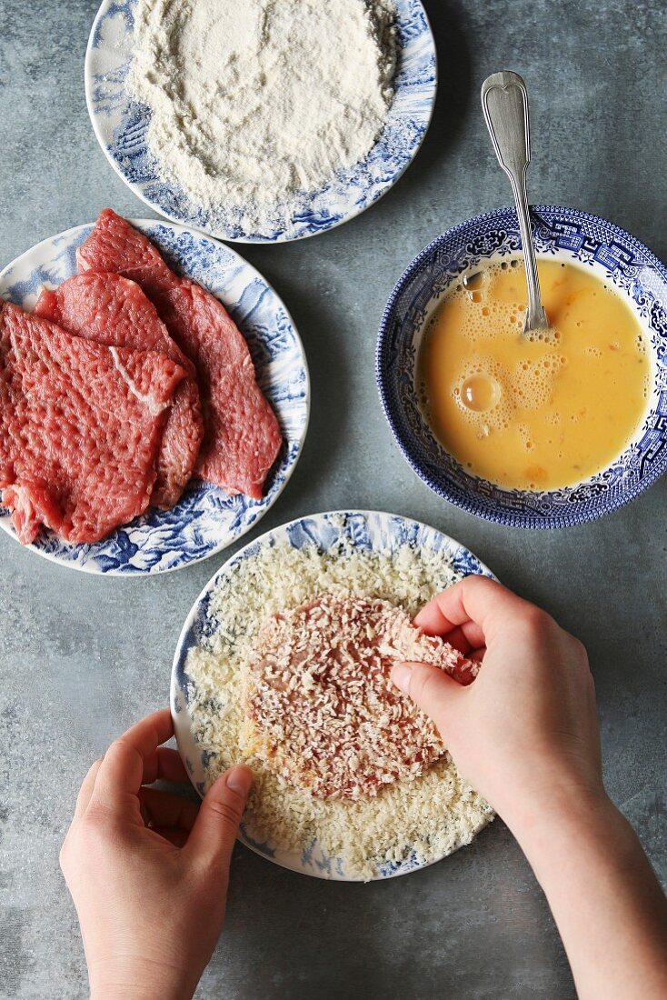 Hände wenden Rindfleisch-Schnitzel in Paniermehl