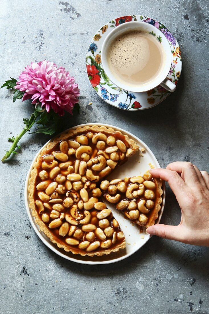 Female hand serving a slice of caramel nut tart with a cup of coffee