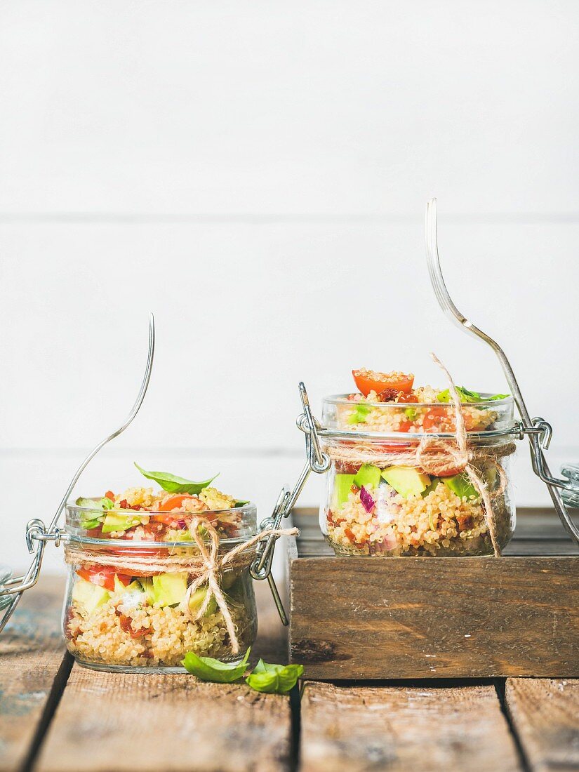 Quinoasalat mit sonnengetrockneten Kirschtomaten, Avocado und Basilikumblättern in Glas
