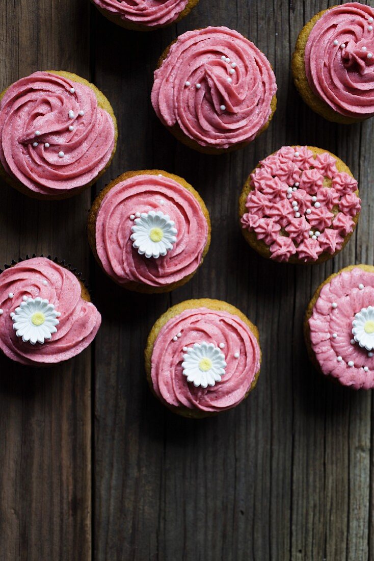 Rosa glasierte Cupcakes mit Zuckerblumen auf Holzuntergrund