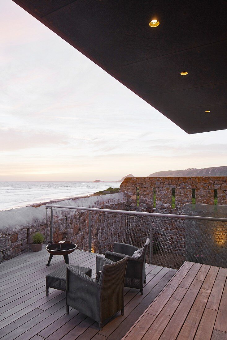 View past armchairs on terrace to sunset over ocean