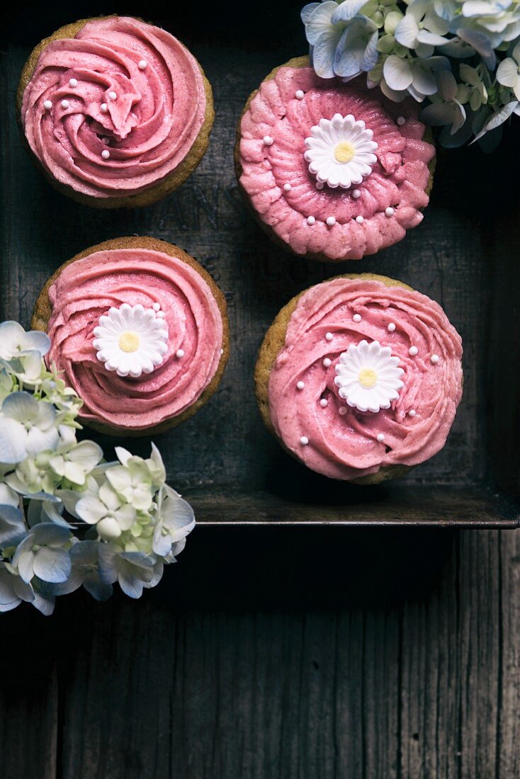 Pink iced cupcakes on a vintage board with flowers