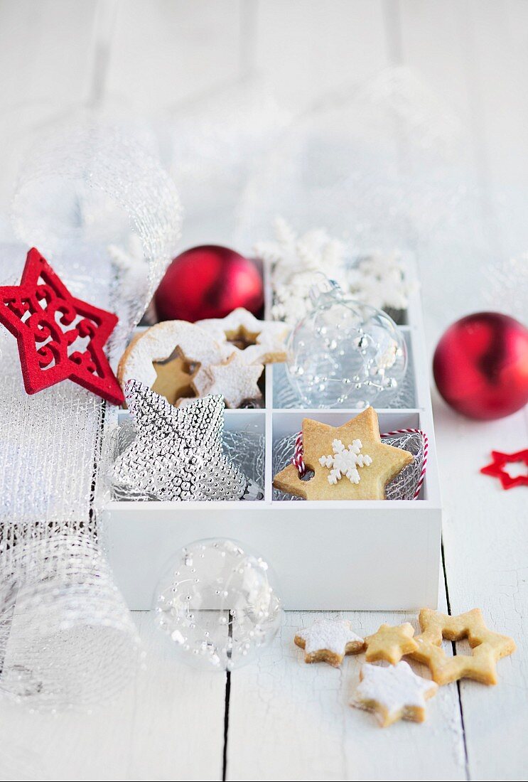 Box mit Weihnachtsplätzchen und Baumanhängern auf weißem Tisch