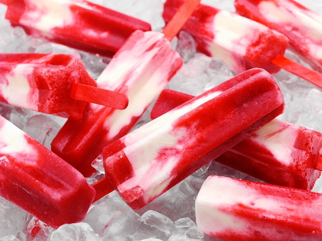 Raspberry and daiquiri cheesecake ice lollies on a bed of ice cubes