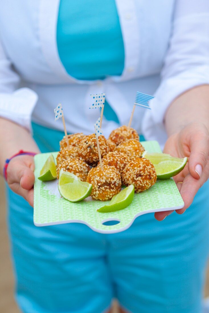 A woman serving fish balls with celery, onion and sesame on a board