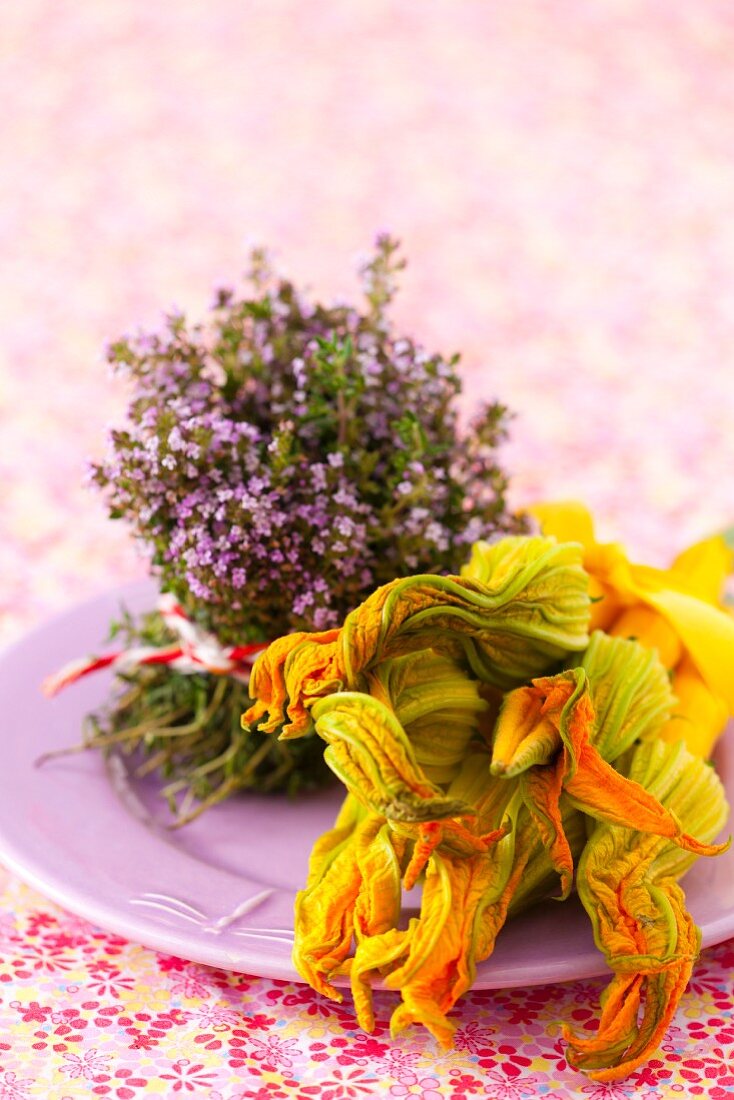 Stillleben mit blühendem Thymian und gelben Zucchini mit Blüten auf Teller