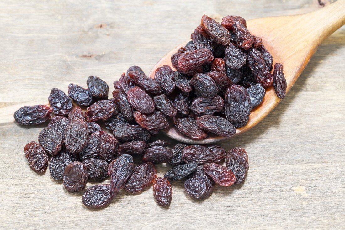 Raisins on a wooden spoon on a wooden board