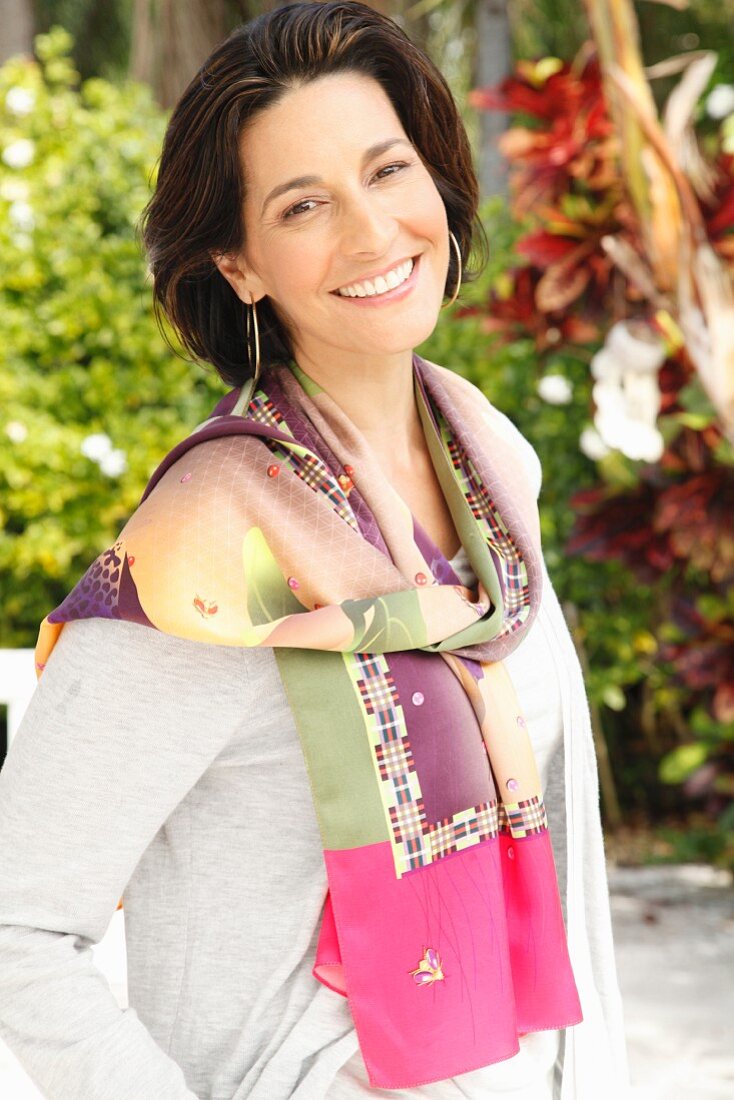 A brunette woman wearing a grey long-sleeved top, hoop earrings and a patterned scarf around her neck