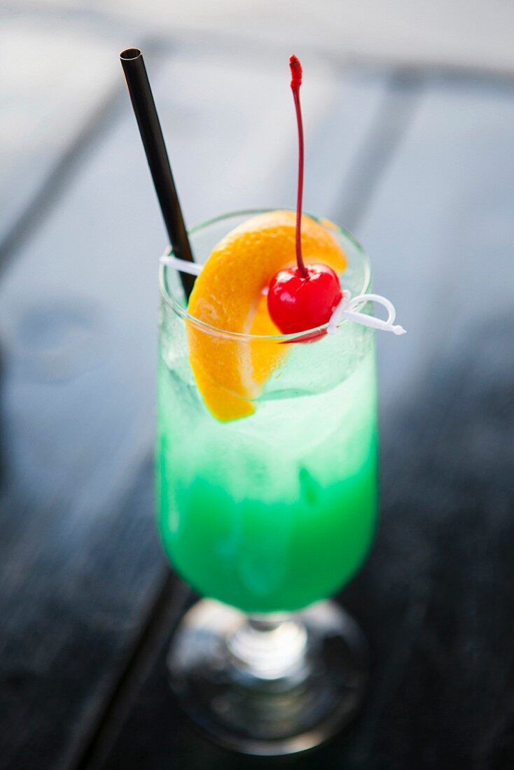 Grüner Cocktail mit Orangenscheibe und Coktailkirsche