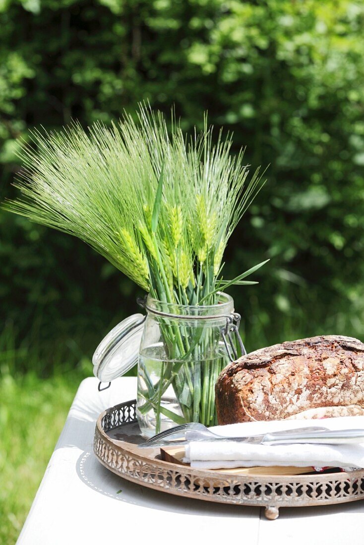 Ears of barley in preserving jar and loaf of bread on table