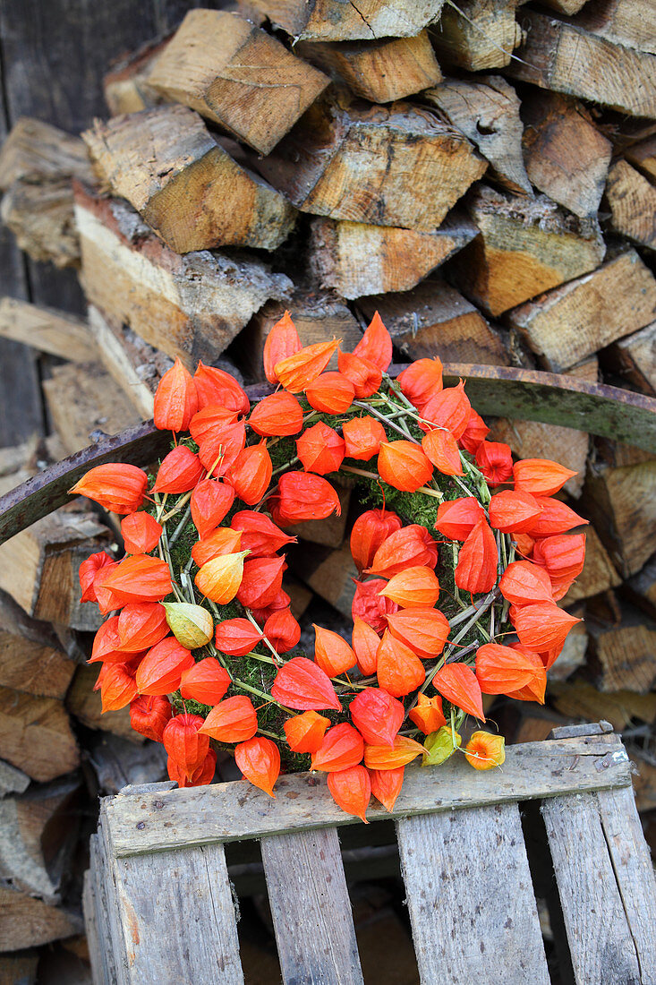 Wreath of moss and physalis on crate in front of stacked firewood