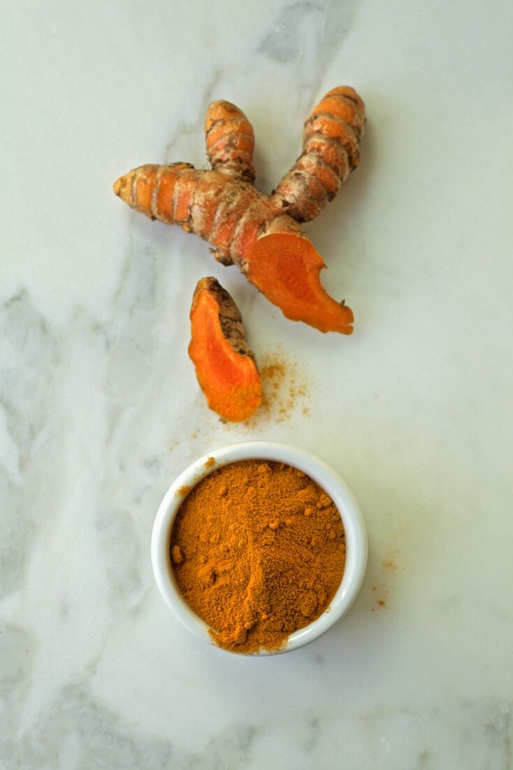 Fresh and ground turmeric on a white marble background