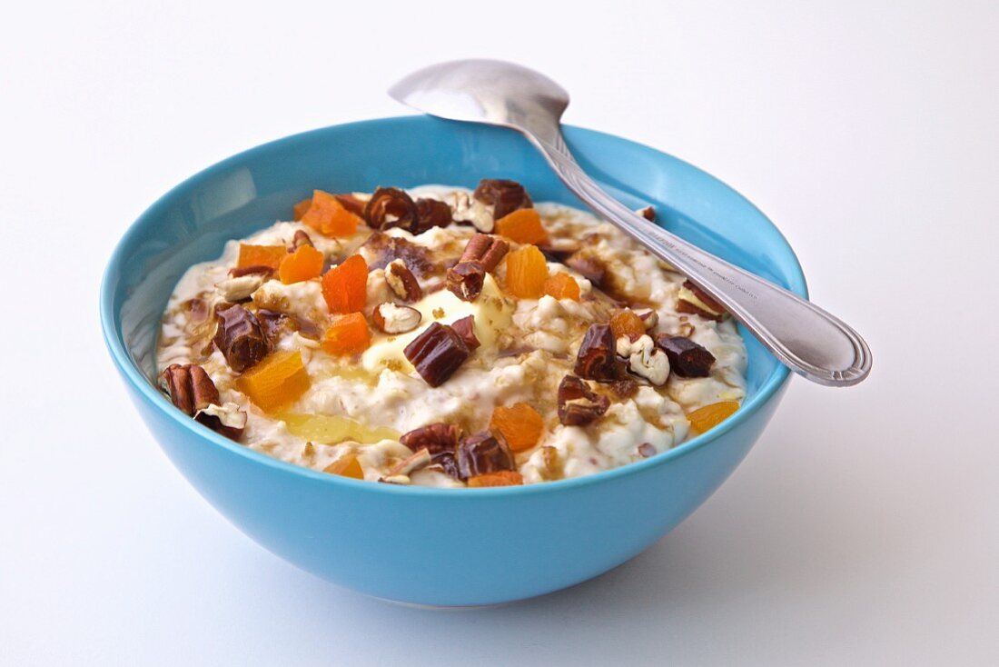 Yogurt with dried fruits, dates, almonds, walnuts, and papaya in a blue bowl on a white background