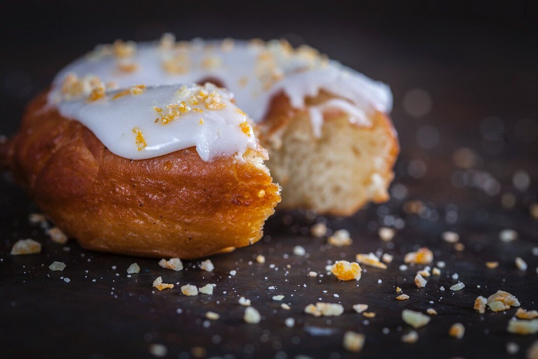 Donut mit Zitronenglasur und kandierten Orangenstücken, angebissen