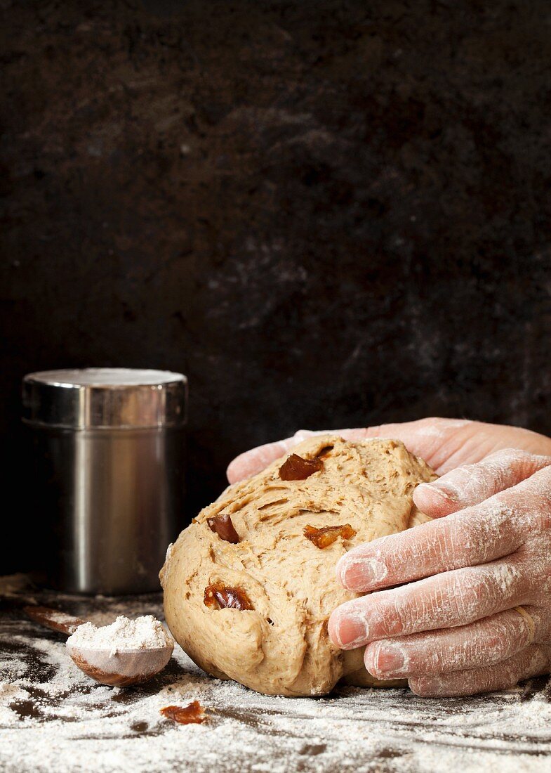 Hands shape rice bread dough with dates into a loaf