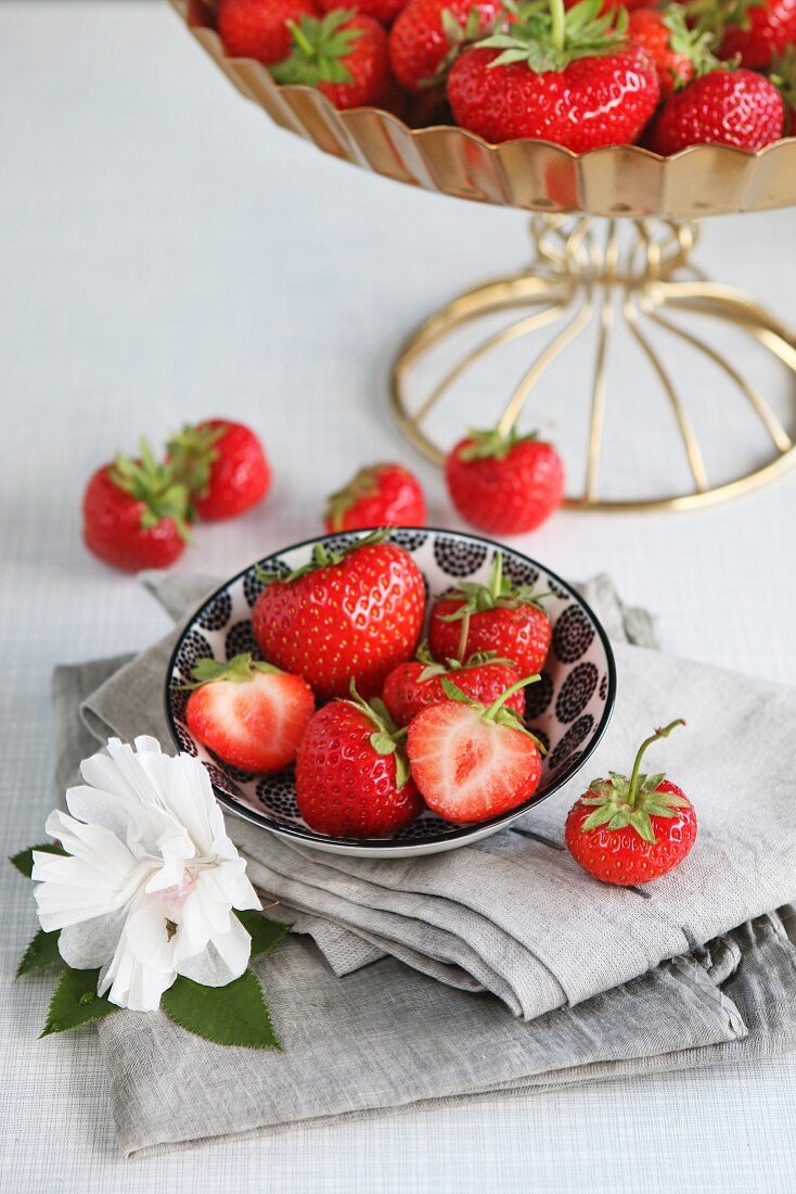 Fresh whole and halved strawberries in a bowl, decorated with a paper flower