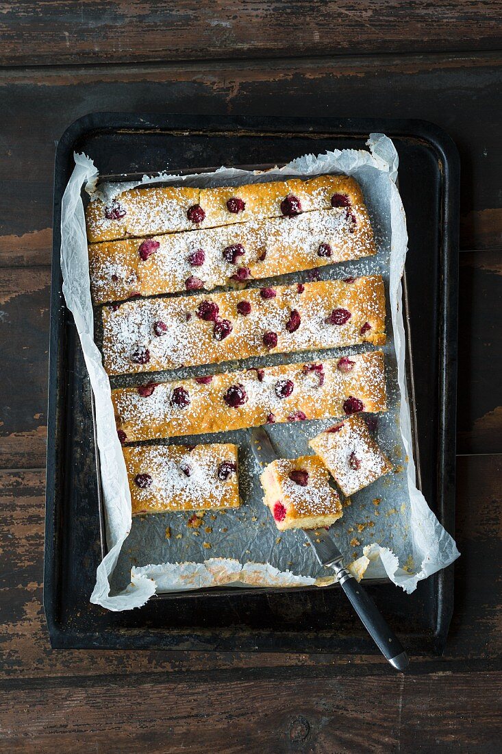 Sponge cake slices with raspberries and icing sugar on a baking tray