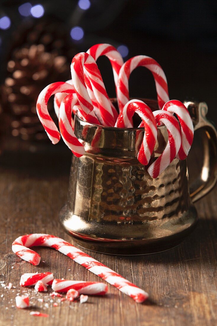 Christmas candy cane in a traditional style gold mug with one whole can on the table with broken candy can pieces