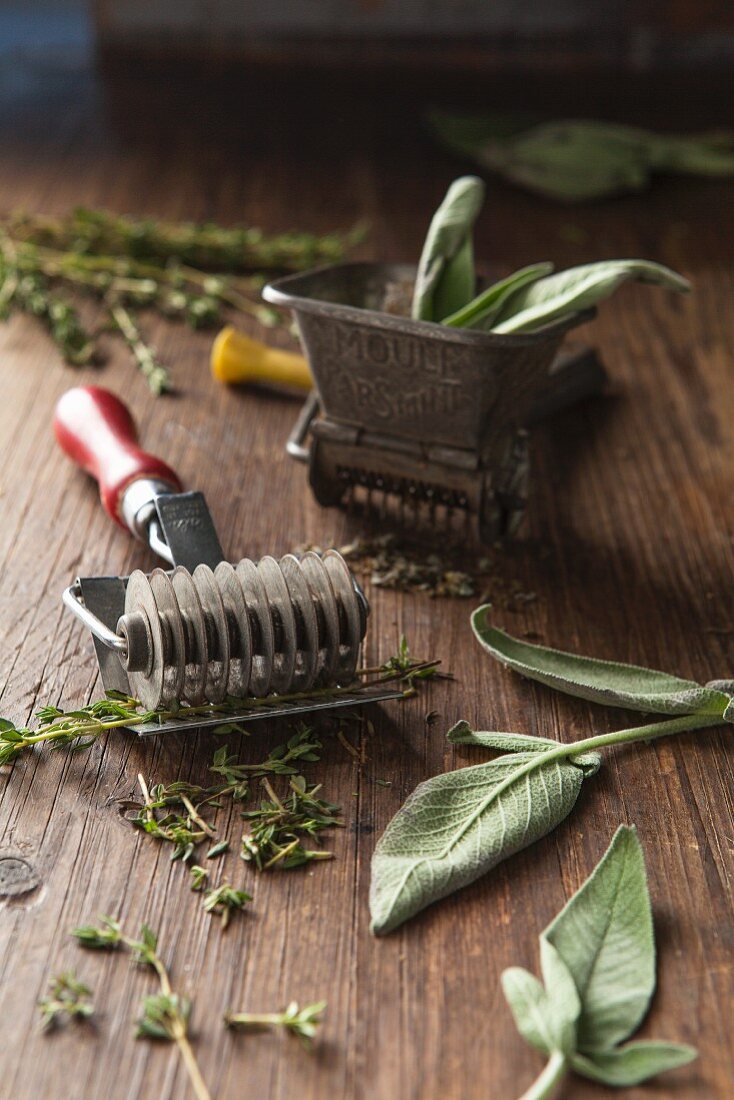 Herb cutter and herb grinder propped with fresh sage and thyme on a wooden surface