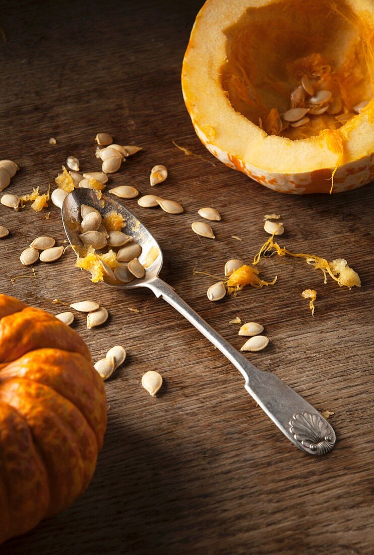 A hollowed out munchkin pumpkin, pumpkin seeds and a vintage spoon on a rustic wooden background