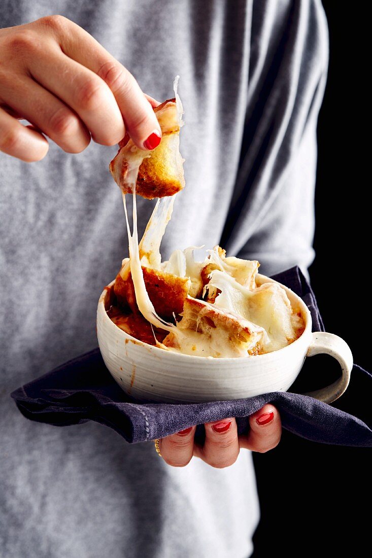 A woman holding a bowl of onion and cheese soup with croutons and bacon